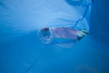 Detail of a volunteer's hand putting a plastic bottle in the bag. Photo taken from below. Concept of Earth Day and World Environment Day June 5.