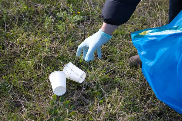 Detail of a volunteer's hand collecting plastic cups from the forest. Concept of Earth Day and World Environment Day June 5.