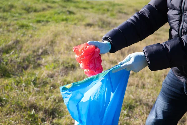 Detail of a volunteer's hand picking up a red plastic bag from the forest and putting it in a garbage bag. Concept of Earth Day and World Environment Day 5 June.