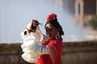 İspanya, Seville 'de ünlü bir meydanda flamenko çingenesi gibi giyinmiş genç siyahi bir kadın. Ruffles ve kırmızı şallı bej bir elbise giyiyor ve kastanetçilik oynuyor. Flamenko kültür mirası.