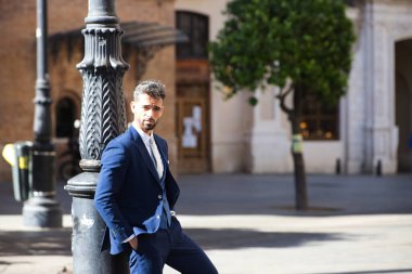 Sakallı, mavi takım elbiseli ve kravatlı yakışıklı bir genç, sokak lambasına yaslanmış, İspanya 'nın Seville şehrinde bir iş gezisinde.