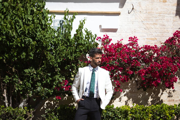 Portrait of handsome young man with beard and white jacket is visiting the city of seville in spain. The man is in a famous square in the district of santa cruz. Travel and holiday concept