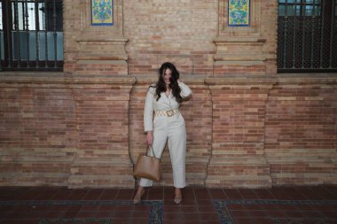 Uzun kahverengi saçlı genç ve güzel kadın Sevilla 'nın en ünlü meydanında. Kadın kırmızı tuğlalardan oluşan bir arka planda farklı duruş ve vücut ifadeleri sergiliyor.