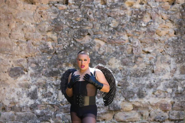Young non-binary Latin person, wearing black make-up and black dress, with black angel wings, covering his chest with his hands. Concept of diversity, homosexuality and human rights