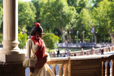 İspanya, Seville 'de bir meydanda flamenko çingenesi gibi giyinmiş genç siyahi bir kadın. O, fırfırlı bej bir elbise ve çiçekli kırmızı bir şal giyer. İnsanlığın Flamenko kültürel mirası. Dans konsepti