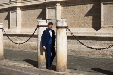 Sakallı, mavi takım elbiseli ve kravatlı yakışıklı bir genç. İspanya 'daki Sevilla katedralinin sütununa yaslanıyor. Bu adam şehirde bir iş gezisinde olan bir yönetici.