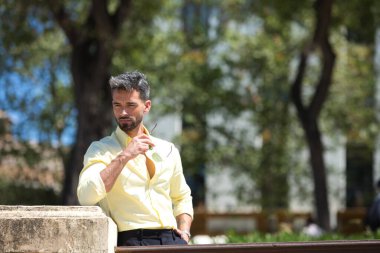 Sakallı, elinde güneş gözlüğü olan yakışıklı genç bir adam korkuluklara yaslanıyor. Adam Sevilla 'da bir bahçede. Seyahat ve tatil konsepti.