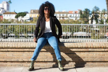 Afro saçlı, kot pantolon ve siyah ceketli, İspanya 'da tatilinin tadını çıkaran genç, güzel siyahi bir kadın. Seyahat ve tatil konsepti.