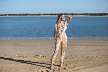 Genç sarışın ve güzel kadın İspanya 'nın güneyindeki kumsalda, kadın mutlu ve saçlarına dokunurken gülümsüyor. Mutluluğu ve sarı günü kavra