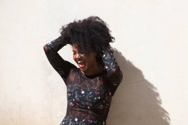 Siyah kadın portresi, genç ve güzel afro saçlı ve çiçekli siyah elbiseli, saçlarına dokunuyor ve eğleniyor, mutlu ve gülümsüyor ve farklı ifadeler takınıyor..