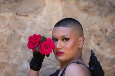 Siyah makyaj ve siyah kanatlar takmış, elinde tuttuğu yüzünün yanında iki kırmızı gülle ikili olmayan genç bir Latin 'in portresi. İfade ve duygu kavramı