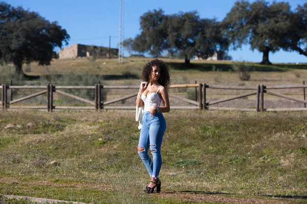 Koyu kıvırcık saçlı, beyaz bluzlu ve kırmızı dudaklı İspanyol kadın güneşli bir günde kırsalda yürüyor..