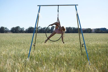 Genç ve güzel sarışın kadın çemberin üzerinde aerobik egzersizleri yapıyor, kadın kırsal kesimde bir buğday tarlasında doğa ile temas halinde. Spor ve sağlık kavramı