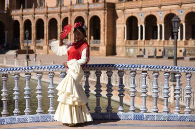 İspanya, Seville 'de ünlü bir meydanda flamenko çingenesi gibi giyinmiş genç siyahi bir kadın. Fırfırlı, kırmızı şallı ve kırmızı vantilatörlü bej bir elbise giyiyor. İnsanlığın Flamenko kültürel mirası