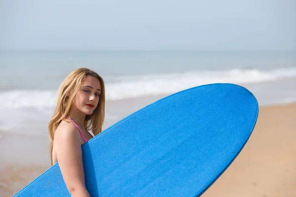 穿着粉色比基尼和蓝色冲浪板的年轻漂亮的金发冲浪女人 这个女孩在海滩上度假以练习她最喜欢的运动 旅行和假日概念 — 图库照片