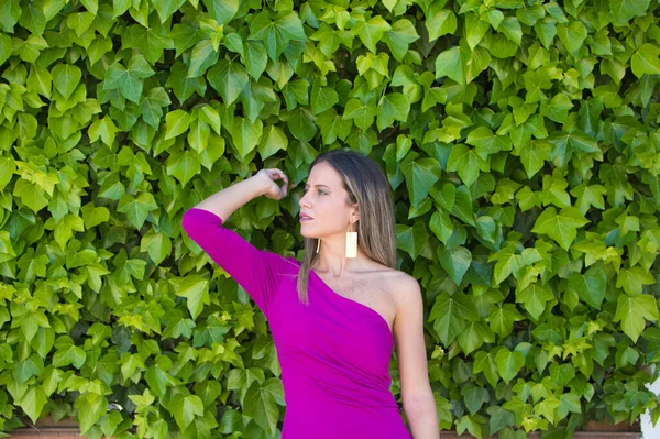 紫のドレスを着た可愛い若いブロンドの女性は ツタの壁を背景に写真をポーズしています 女性は異なる表現をします — ストック写真