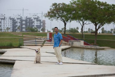 Sakallı ve Labrador av köpeği olan yakışıklı genç bir adam. Parktaki gölde fotoğraf çekmek için poz veriyor. Adam evcil hayvanına sevgisini okşayarak, öpücüklerle ve sarılmalarla gösterir. Evcil hayvanlar.