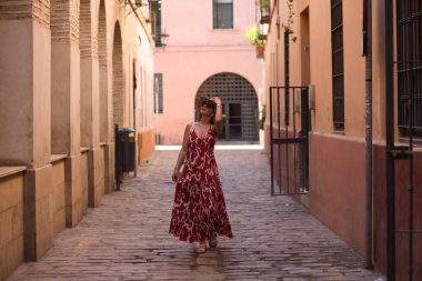 Genç ve güzel sarışın kadın, güneş gözlüğü ve kafasında hasır bir şapkayla Seville 'in tarihi merkezinde yürüyor. Kadın tatilde ve şehrin tadını çıkarıyor. Kadın mutlu.