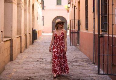 Genç ve güzel sarışın kadın, güneş gözlüğü ve kafasında hasır bir şapkayla Seville 'in tarihi merkezinde yürüyor. Kadın tatilde ve şehrin tadını çıkarıyor. Kadın mutlu.