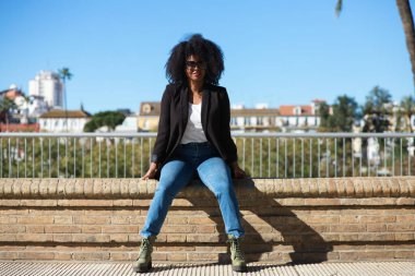 Afro saçlı, kot pantolon ve siyah ceketli, İspanya 'da tatilinin tadını çıkaran genç, güzel siyahi bir kadın. Seyahat ve tatil konsepti.