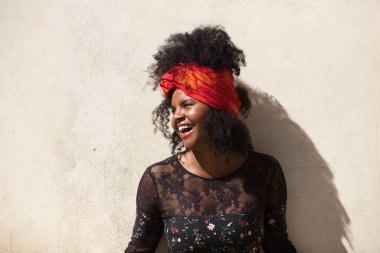 Genç, güzel, siyah bir kadının portresi, afro saçlı, çiçekli siyah elbiseli, saçında kırmızı bir eşarp olan. Kadın mutlu, gülüyor ve eğleniyor. Farklı ifadeleri kavra