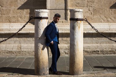 Sakallı, mavi takım elbiseli ve kravatlı yakışıklı bir genç. İspanya 'daki Sevilla katedralinin sütununa yaslanıyor. Bu adam şehirde bir iş gezisinde olan bir yönetici.