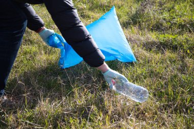 Hand detail of a volunteer collecting plastic bottle from the forest to put in the recycling bag. Concept of Earth Day and World Environment Day June 5.
