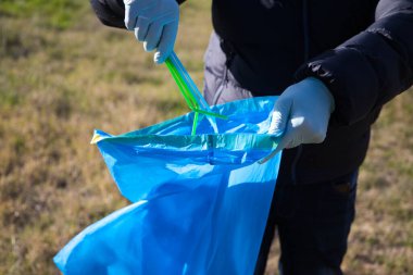 Ormandan plastik çubukları alıp plastik torbaya koyan bir gönüllü elinin ayrıntıları. Dünya Günü ve Dünya Çevre Günü kavramı 5 Haziran.