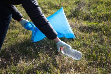 Hand detail of a volunteer collecting plastic bottle from the forest to put in the recycling bag. Concept of Earth Day and World Environment Day June 5.