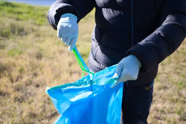 Detail of a volunteer\'s hand picking up plastic straws from the forest and putting them in the plastic bag. Concept of Earth Day and World Environment Day June 5.