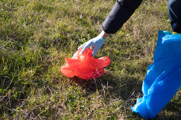 Detail of a volunteer\'s hand picking up a red plastic bag from the forest. Concept of Earth Day and World Environment Day June 5.