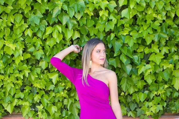 紫のドレスを着た可愛い若いブロンドの女性は ツタの壁を背景に写真をポーズしています 女性は異なる表現をします — ストック写真