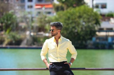 Sevilla 'daki Guadalquivir nehrinin korkuluklarına yaslanmış sakallı ve güneş gözlüklü yakışıklı genç adam. Diğer kıyıda, Sevilla 'nın ünlü Flamenko sanatçıları mahallesi var..