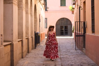 Genç ve güzel sarışın kadın, güneş gözlüğü ve kafasında hasır bir şapkayla Seville 'in tarihi merkezinde yürüyor. Kadın tatilde ve şehrin tadını çıkarıyor. Kadın mutlu.