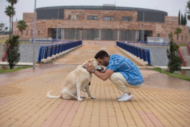 Sakallı ve Labrador köpeği dinlenmek için duran yakışıklı genç adam. Adam köpeğe sevgi ve sevgiyle bakar ve yüzlerini birbirine yaklaştırırlar. Evcil hayvanlar ve hayvanlar.