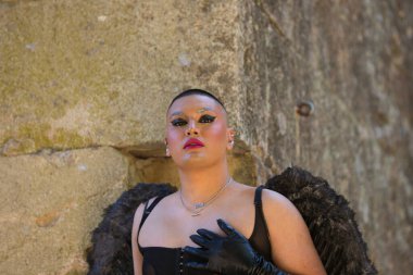 Siyah makyaj ve siyah kanatlar takan, ortaçağ şatosunda gargoyle kılığına girmiş, ikili olmayan genç bir Latin 'in portresi. Çeşitlilik, eşcinsellik ve insan hakları kavramı