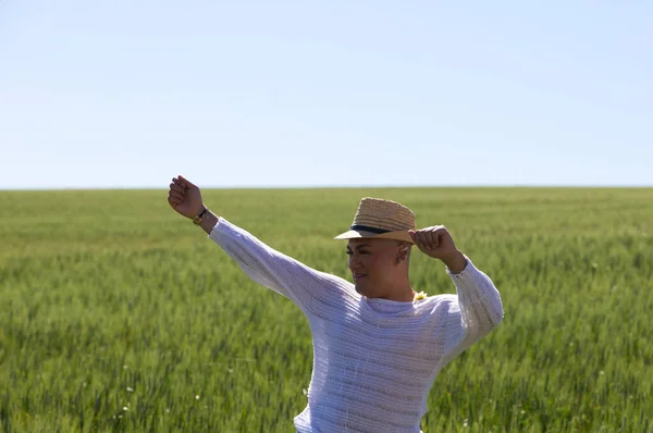 A young non-binary gay Latin person wearing a straw hat and having fun in the green wheat field doing different body postures with his hands and arms. Concept of diversity and homosexuality.
