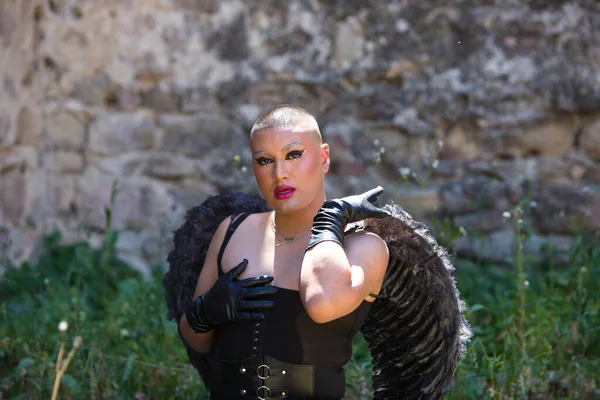 Young non-binary Latin person, wearing black make-up and black angel wings and making different expressions with his face and hands. Concept of expressions and emotions.