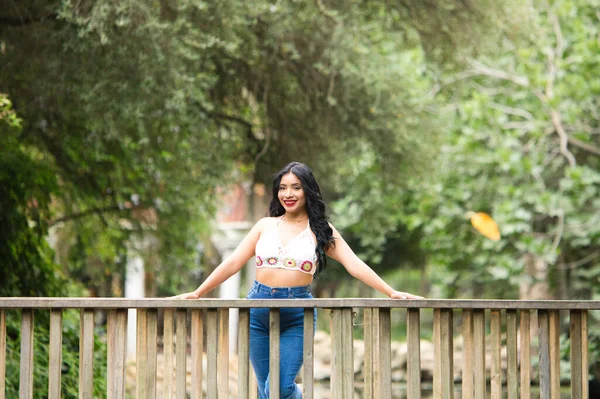 Genç ve güzel esmer kadın ve Latin, ördeğin üzerindeki ahşap köprünün korkuluğuna yaslanıyor ve parktaki balık göletine yaslanıyor. Kadın gülümsüyor, mutlu ve günün tadını çıkarıyor..