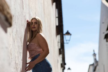 Genç, güzel, mavi gözlü sarışın kadın duvara yaslanıyor ve gündelik, modern kıyafetler giyiyor. Kadın yüzüyle farklı ifadeler kullanıyor, gülümsüyor, ciddi, mutlu ve üzgün.