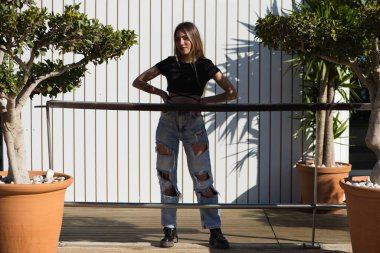 Genç, güzel sarışın kadın yırtık kot pantolon ve siyah bluz giyiyor. Arka planda beyaz ahşap kulübe. Kadın makyaj malzemesi giyiyor. Yaşam tarzı, güzellik ve moda konsepti