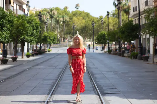Young and beautiful blonde woman from the United States is on a sightseeing trip to Seville, Spain. The woman is enjoying her holidays in europe. She is between the rails of the urban tram