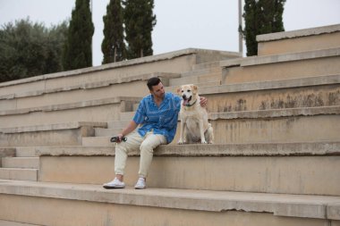 Sakallı ve Labrador köpeği tribünde dinlenmek için duran yakışıklı genç adam. Evcil hayvanlar ve hayvan yoldaşları. Uluslararası köpek günü.