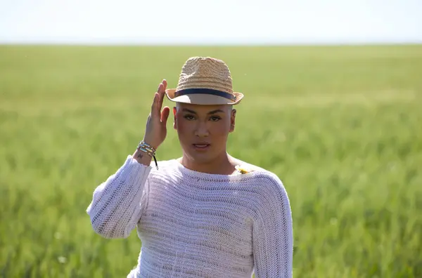 Portrait of a young non-binary latin person wearing a straw hat and standing in the green wheat field making different expressions. Concept of diversity, homosexuality and human rights.
