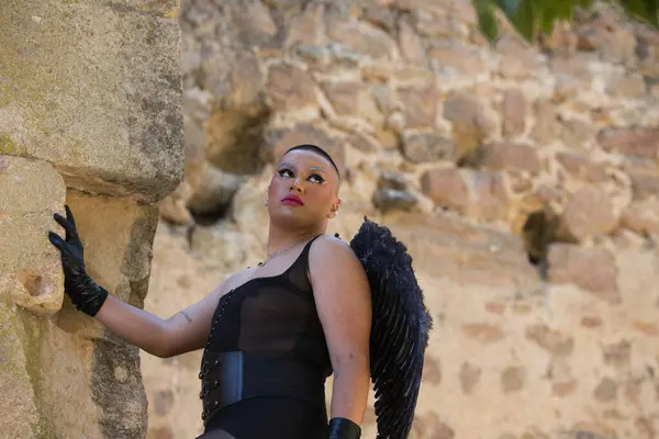 Portrait of a young non-binary latin person, wearing black make-up and black wings, posing as a gargoyle in a medieval castle. Concept of diversity, homosexuality and human rights