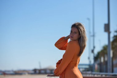 Deniz kıyısındaki balıkçıların teknelerinde oturan güzel sarışın kadın. Ufuktaki arka planda mavi deniz ve denizde çalışan tekneler. Tatil ve seyahat kavramı