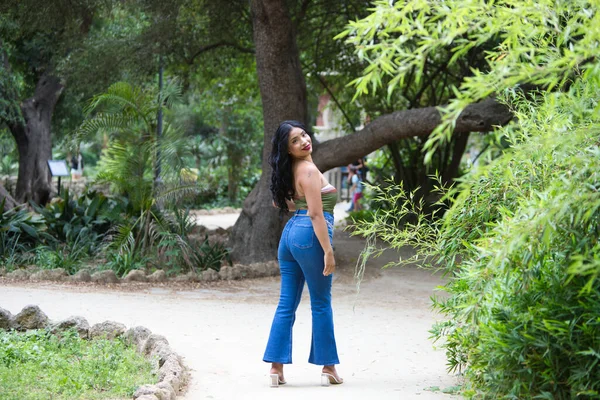Young and beautiful brunette woman, latin from south america walks among the trees and vegetation of the park. The woman is smiling and happy and is posing with her back to the photos.
