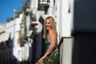 Genç, güzel, mavi gözlü sarışın kadın duvara yaslanıyor ve gündelik, modern kıyafetler giyiyor. Kadın yüzüyle farklı ifadeler kullanıyor, gülümsüyor, ciddi, mutlu ve üzgün.