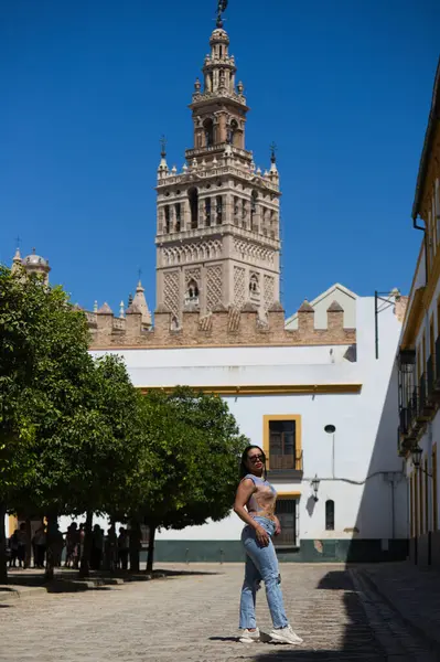Young and beautiful brunette woman, latin and with sunglasses, dresses casually. The girl is on holiday in seville. In the background the cathedral of seville and the giralda tower. Travel concept