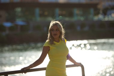 Seville 'deki nehrin kenarındaki korkuluklara yaslanan güzel sarışın kadın. Kadın sarı bir elbise giyiyor ve İspanyol şehrinde günün tadını çıkarıyor. Seyahat ve tatil konsepti